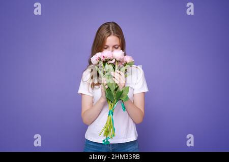 Ritratto ragazza allegra con romantico bouquet primavera peonie rosa su sfondo viola studio. La ragazza gorgeous gode la celebrazione di giorno delle donne e riceve i fiori come regalo speciale Foto Stock