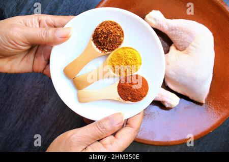 Mani che tengono il piatto di pepe di cayenne, curcuma, paprika su cucchiaio di legno. Foto isolare su sfondo grigio vista dall'alto Foto Stock