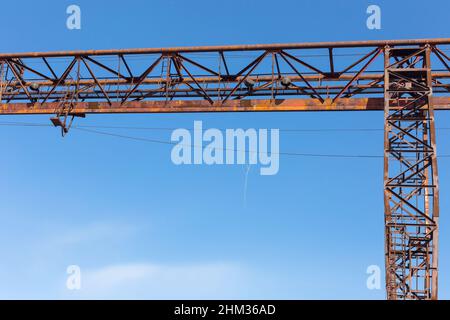 Vecchia gru a portale arrugginita sulla ferrovia, una pianta di cemento abbandonata. La crisi, il crollo dell’economia e la chiusura delle capacità produttive hanno portato al confronto Foto Stock