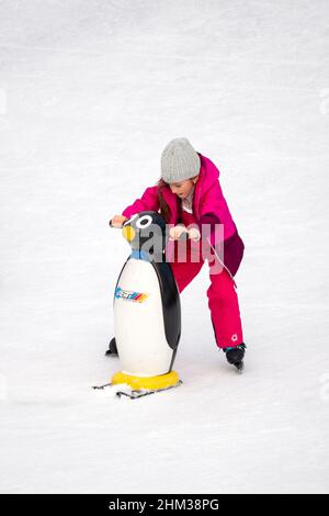 Lone bambina imparando a pattinare sul ghiaccio utilizzando sci pinguino ghiaccio skating aid Foto Stock