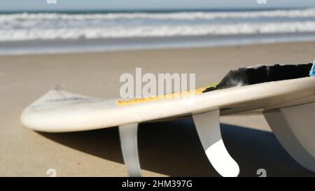 Surfboard per il surf sdraiato sulla spiaggia di sabbia, costa californiana, USA. Onde oceaniche e tavole da surf bianche o paddleboard. Longboard o sup per la ricreazione di sport acquatici con acqua di mare. Cinematografia senza giunture. Foto Stock