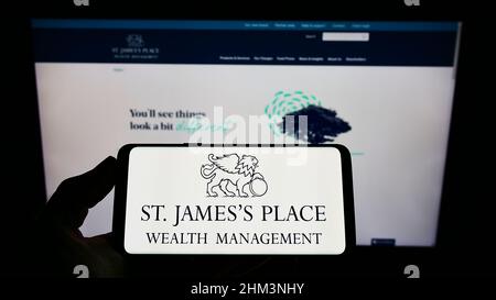 Persona che tiene uno smartphone con il logo della società britannica St. James's Place plc sullo schermo di fronte al sito web. Mettere a fuoco sul display del telefono. Foto Stock