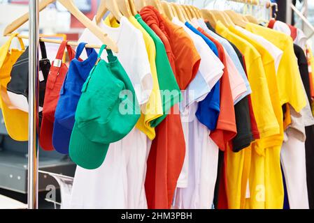 T-shirt e cappellini colorati sull'appendiabiti nel negozio Foto Stock