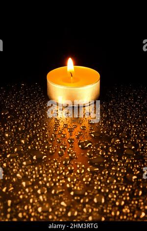 Candela di cera su sfondo scuro circondata da gocce d'acqua, primo piano sfocato Foto Stock