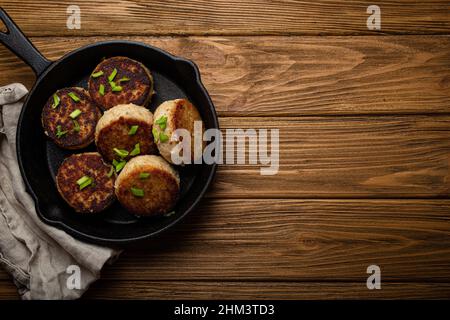 Cotolette fatte in casa di pesce, pollo o carne su padella in ghisa nera Foto Stock