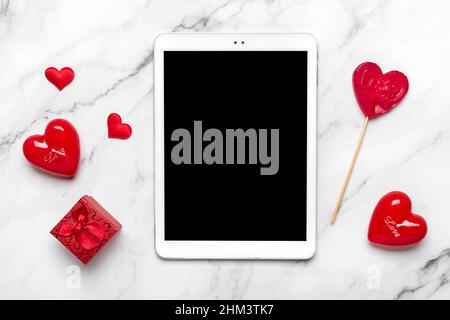 Tablet per scegliere regali, fa l'acquisto, busta, scatola, due cuori rossi sul tavolo di marmo Vista dall'alto Flat Lay Lista di acquisti di Vacanza, buon San Valentino Foto Stock
