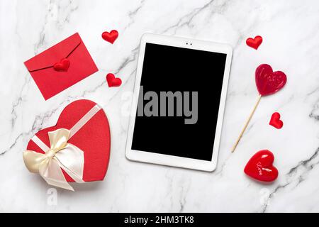 Tablet per scegliere regali, fa l'acquisto, busta, scatola, due cuori rossi sul tavolo di marmo Vista dall'alto Flat Lay Lista di acquisti di Vacanza, buon San Valentino Foto Stock