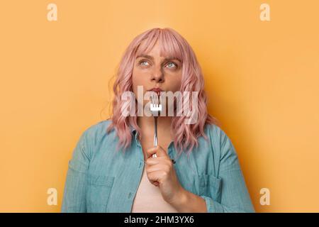 Ritratto di donna affamata che tiene la forcella isolato su sfondo giallo parete. Concetto di assistenza sanitaria Foto Stock