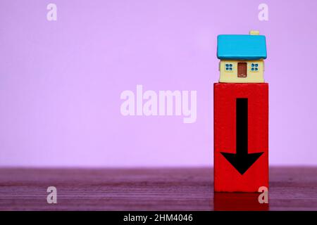 Crisi del mercato immobiliare, concetto di calo dei prezzi. Casa in miniatura e cubo di legno rosso con freccia rivolta verso il basso. Foto Stock