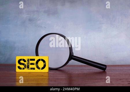 Concetto di ottimizzazione dei motori di ricerca. Lente d'ingrandimento e cubo di legno con testo SEO o ottimizzazione di Search Engine Foto Stock