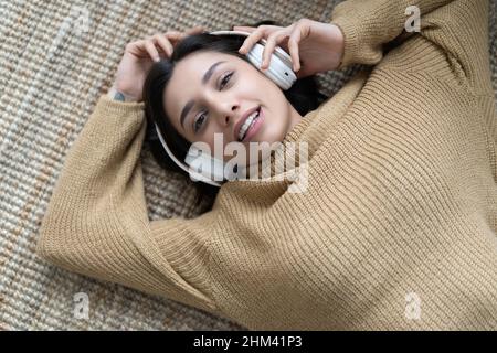 Ritratto di una donna rilassata che ascolta la musica con le cuffie sdraiate su un tappeto a casa Foto Stock