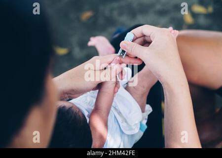 Mano della madre che tiene il suo pollice del bambino di un mese vecchio per tagliare le sue unghie per la prima volta. Scatto in testa. Foto Stock