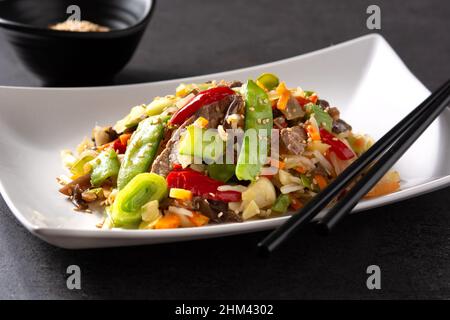 Manzo, verdure e semi di sesamo in piatto bianco su sfondo nero Foto Stock