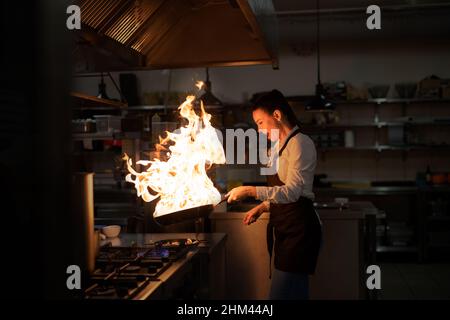 Chef professionista che prepara il pasto, flambing al coperto nella cucina del ristorante. Foto Stock