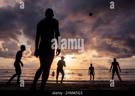 Silhouette sulla spiaggia di Beau Vallon che gioca a pallavolo al tramonto sull'isola di Mahe, Seychelles. Foto Stock