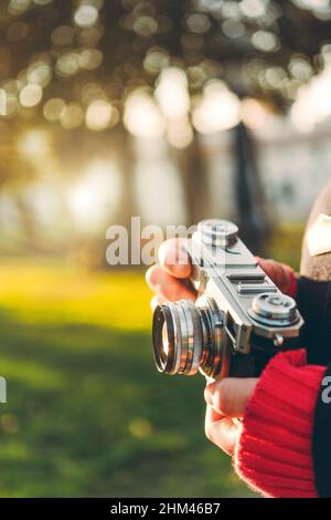 Primo piano della mano della donna che tiene la macchina fotografica vintage nella foresta con il tempo di sole. Foto Stock