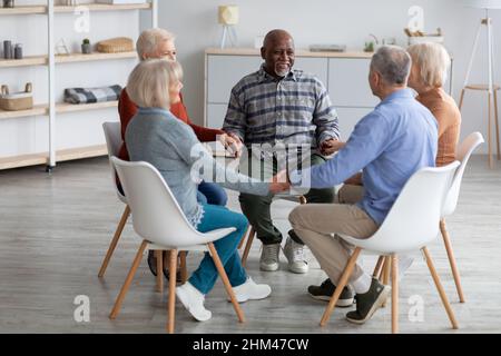 Gruppo multirazziale di pensionati felici seduti in cerchio, con le mani in mano Foto Stock