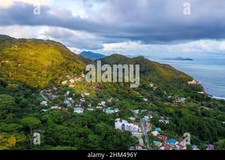 Mahe Island con Port Glaud villaggio paesaggio drone, con lussureggiante foresta tropicale del Parco Nazionale Morne Seychellois e Oceano Indiano all'orizzonte. Foto Stock