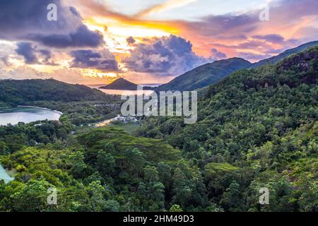 Mahe Island costa drone tramonto paesaggio con drammatico cielo rosa, nuvole, lussureggiante foresta tropicale e piccole isole intorno. Foto Stock