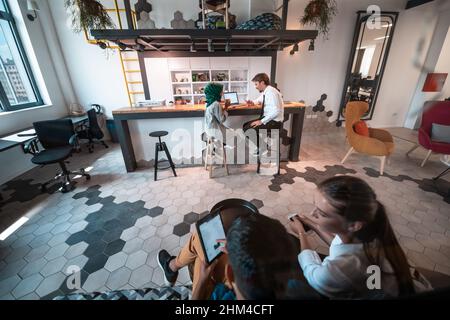 Gruppo di uomini d'affari multietnici occasionali che si prendono pausa dal lavoro facendo cose diverse mentre si gode il tempo libero nella zona relax al moderno Foto Stock