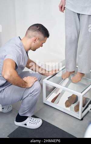 Dottore che controlla le suole dei piedi della donna nello specchio Foto Stock