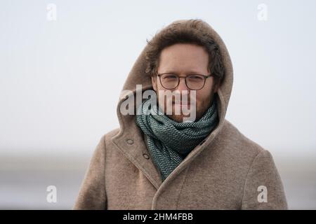 07 febbraio 2022, Schleswig-Holstein, Nordstrand: Jan Philipp Albrecht (Bündnis 90/Die Grünen), ministro della transizione energetica, dell'agricoltura, dell'ambiente, della natura e della digitalizzazione, si trova su una diga delle coste del Mare del Nord durante un briefing mediatico sulla strategia di protezione delle coste. In considerazione del previsto aumento dei livelli del mare e di forti picchi di tempeste, il proseguimento del programma di rafforzamento della diga riveste particolare importanza per lo stato dello Schleswig-Holstein. Secondo il ministero, circa un quarto della superficie dello Schleswig-Holstein è potenzialmente a rischio di picchi di tempesta. Più di 330, Foto Stock