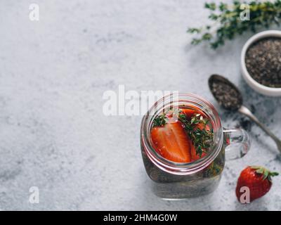 Vista da sopra chia acqua in mason jar con fragola e timo sul cemento grigio Sfondo. Chia infusa detox acqua con bacche. Copia spazio per il testo. Mangiare sano, bevande, dieta detox concept Foto Stock