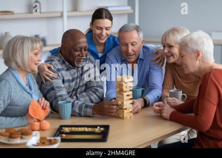 Gente anziana allegra che paga jenga alla sede di cura Foto Stock