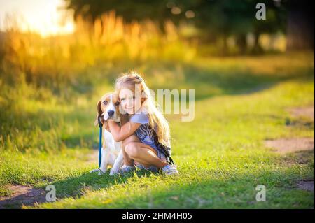 carina ragazza cammina con il suo cucciolo beagle nel parco al tramonto, migliore amico Foto Stock