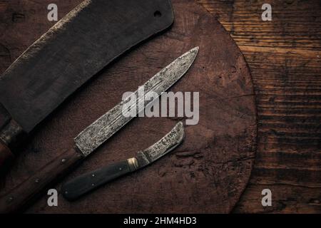 tre utensili da taglio di carne d'epoca su un vecchio tagliere di legno sul piano del tavolo Foto Stock