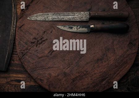 due coltelli vintage su un vecchio tagliere rotondo di legno vicino ad una lama di taglio , vista dall'alto con spazio di copia Foto Stock