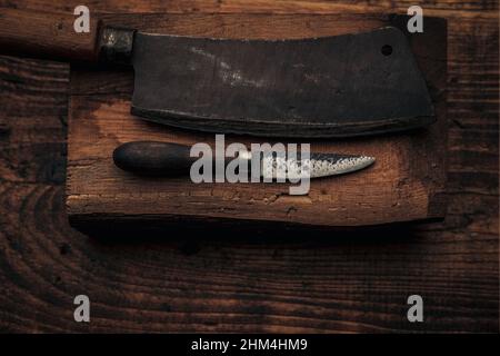 tagliando o disossando, potete scegliere il vostro utensil per la vostra carne - coltello piccolo vicino al cliver su un tagliere di legno Foto Stock