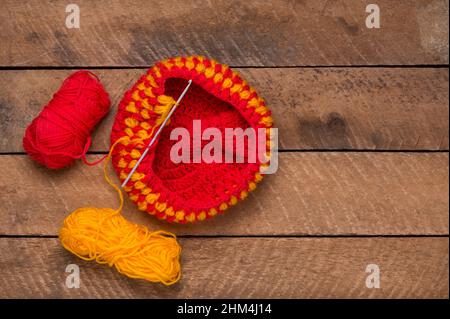 tessuto di lana per maglieria con l'ago, filo tessuto rosso e giallo su un piano di tavolo, concetto di maglieria e lavorazione, spazio copia Foto Stock