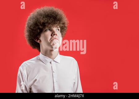 Un bell'uomo con capelli ricci in una camicia fa un gesto del labbro. Non male. Foto Stock