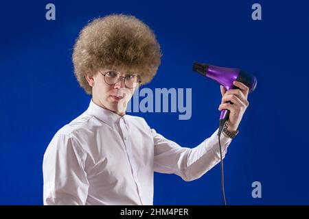 Bell'uomo dai capelli rossi che tiene in mano un asciugacapelli. Capelli bellissimi. Dirigete l'aria verso di voi. Per asciugare i capelli. Shaggy ragazzo. Perdente. Umorismo. Divertimento Foto Stock