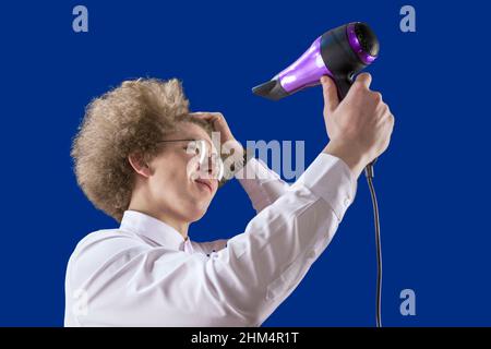 Perdente. Shaggy ragazzo. Dirigete l'aria verso di voi. Bell'uomo dai capelli rossi che tiene in mano un asciugacapelli. Capelli bellissimi. Per asciugare i capelli. Umorismo. Divertimento Foto Stock