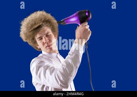 Umorismo. Divertente studente. Capelli bellissimi. Shaggy ragazzo. Dirigete l'aria verso di voi. Perdente. Bell'uomo dai capelli rossi che tiene in mano un asciugacapelli. T Foto Stock