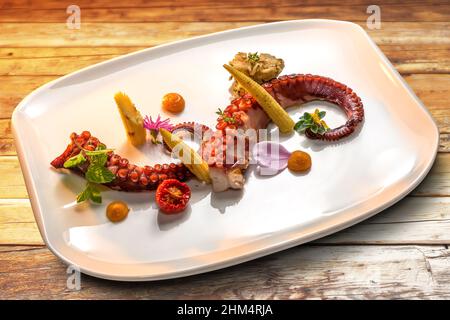 Tentacoli di polpo arrostiti con mais giovane, pomodoro e foglie di menta in piatto bianco su tavole di legno Foto Stock