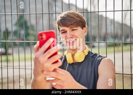 Allegro sportivo giovane che fa videochiamata sul suo smartphone con auricolare - giovane uomo vestito prendere un selfie dopo l'allenamento Foto Stock