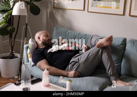 Padre che si rilassa con il bambino sul divano Foto Stock