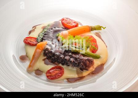 Tentacolo di polpo stufato di vino rosso su purè di patate con asparagi, carota, finocchio e pomodoro. Primo piano nella lastra di vetro Foto Stock