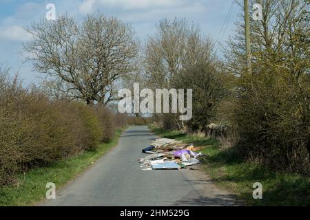 Ribaltamento a volo dei rifiuti domestici, tra cui vetro e legno che si sparge su una strada di campagna stretta e quasi ostruendo Foto Stock