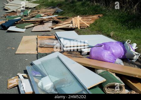 Vista ravvicinata dei rifiuti domestici dispersi incautamente e quasi ostruendo una stretta strada di campagna causando un grave pericolo per gli altri conducenti. Foto Stock