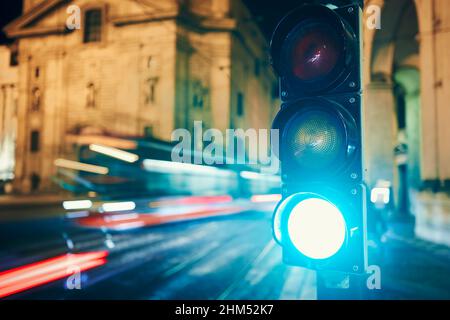 Verde al semaforo contro tram e auto in movimento sfocato. Scena notturna di strada della città a Praga, Repubblica Ceca. Foto Stock