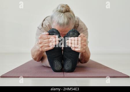 Donna attiva senior che tiene i piedi mentre si piega in avanti e mantiene la testa su gambe allungate mentre si esegue yoga asana Foto Stock