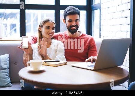 Uomo e donna sorridenti che guardano il video sul portatile in un'accogliente caffetteria Foto Stock