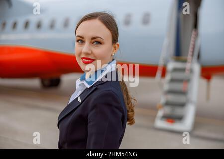 Gioioso assistente di volo donna in piedi all'aperto in aeroporto Foto Stock