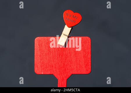 Placca di legno rossa, superficie con cuore attaccato su un chiodo di garofano. Luogo per il testo, mock-up. Sfondo nero. Foto Stock