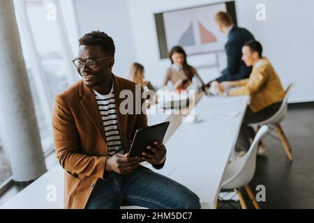 Bel giovane uomo d'affari afroamericano che lavora con un tablet digitale davanti ai suoi colleghi nella sala riunioni Foto Stock