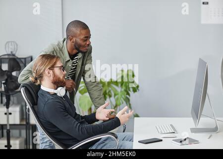 Due giovani programmatori contemporanei che discutono i dati sullo schermo del computer mentre uno di loro fa la presentazione Foto Stock